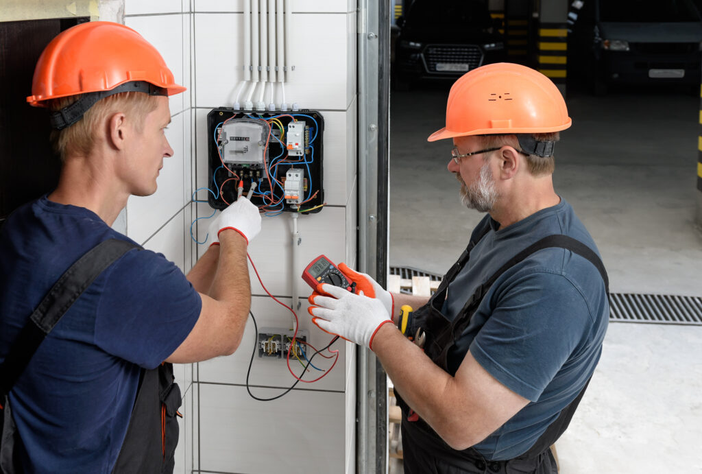 Electricians are checking the voltage at the terminals of the electrical meter. They are using a multimeter.